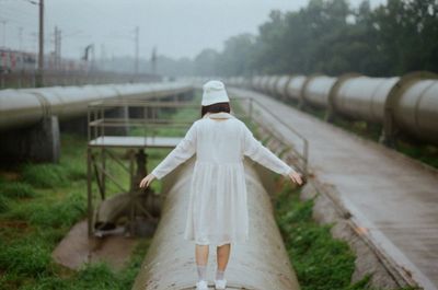 Rear view full length of young woman standing with arms outstretched on pipe