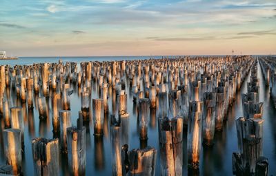 Wooden posts in sea against sky during sunset