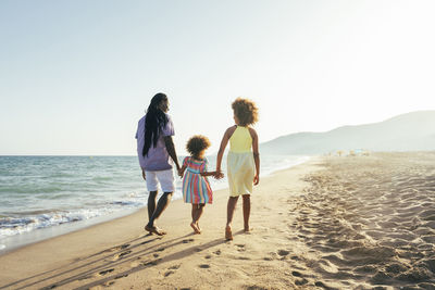 Man with daughters walking at beach on sunny day