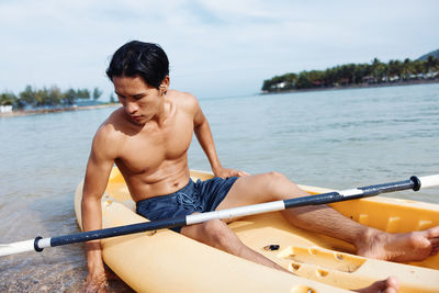 Portrait of shirtless man kayaking in lake