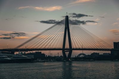 View of suspension bridge over river against cloudy sky