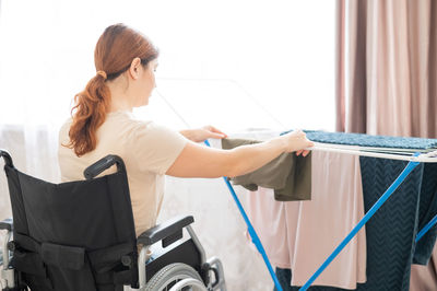 Rear view of woman doing chores sitting on wheelchair