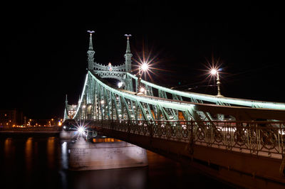 Illuminated bridge over river against sky at night