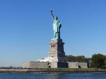 Statue of liberty by hudson river against blue sky