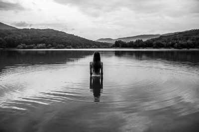 Rear view of person standing in lake against sky