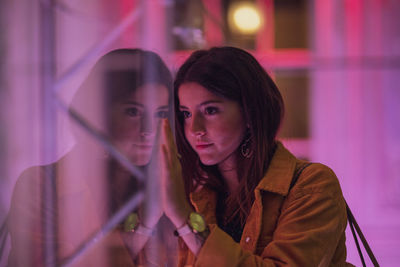 Young woman looking away while standing by glass window