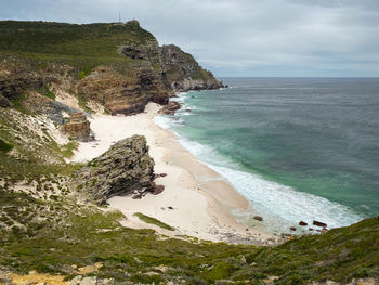 Scenic view of dias or diaz beach with yellow fynbos flower and sea against sky 