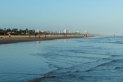 People on beach against clear blue sky