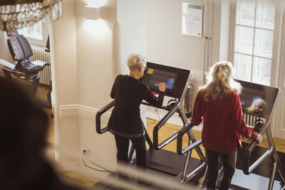 Rear view of senior female friends exercising on treadmill at retirement home