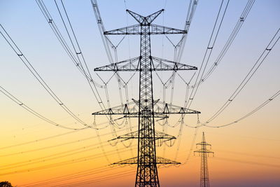 Low angle view of electricity pylon against sky during sunset