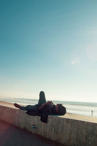 Man sitting on beach against clear sky