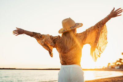 Rear view of woman with arms raised standing at beach