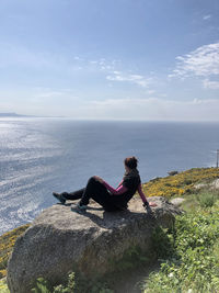 Woman sitting on rock by sea against sky