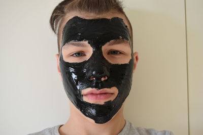 Close-up portrait of teenage boy with black facial mask against wall