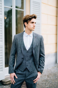 Young man looking away while standing against wall