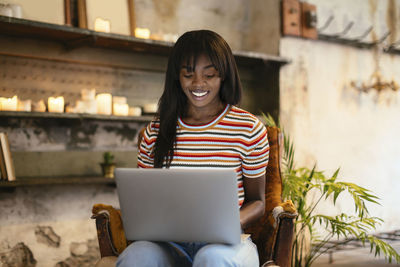 Portrait of smiling young woman sitting on leather chair using laptop