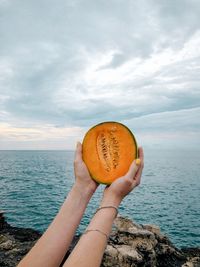 Person holding ice cream cone against sea