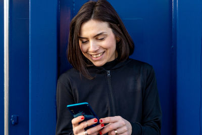 Young adult female runner is using smartphone among the shipping containers of a commercial port