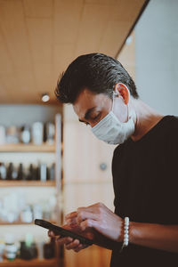 Young man wearing surgical protection mask seriously when his checking smartphone