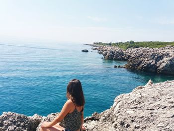 Rear view of woman standing on rock by sea against clear sky