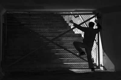 Rear view of man standing by chainlink fence by staircase