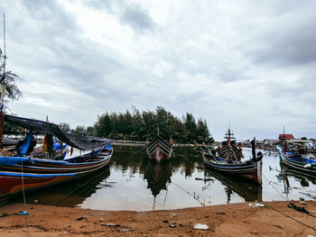 Boats moored in river against cloudy sky