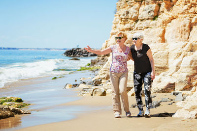 Two elderly women are walking along the rocky shore