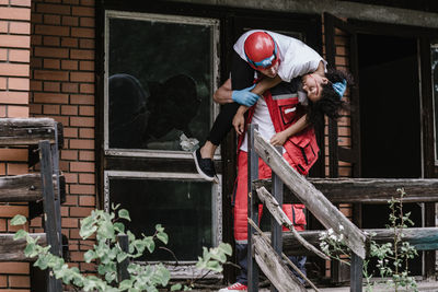 Rescue worker carrying disaster victim out of damaged house