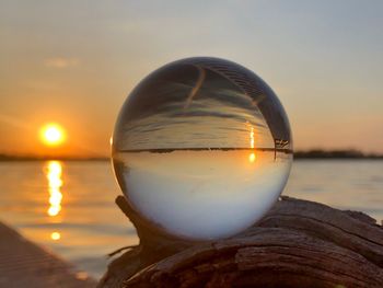 Close-up of crystal ball in sea against sky during sunset