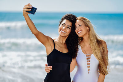 Happy female friends taking selfie while standing at beach