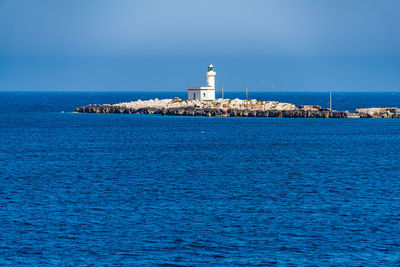 Lighthouse by sea and buildings against blue sky