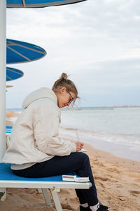 Young woman artist painting or doing travel sketches using watercolor by the seaside