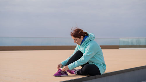 Full length of woman tying shoelace on promenade