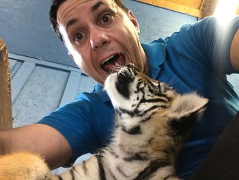 Low angle view of male care taker with tiger cub at zoo