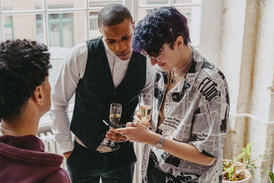 Non-binary person sharing smart phone with businessman holding drink glass during event at convention center