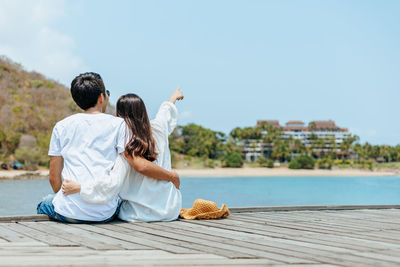 Rear view of couple sitting on shore against sky