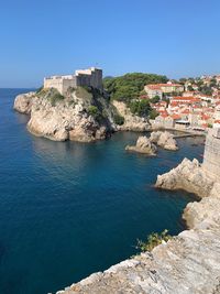 Buildings by sea against clear blue sky