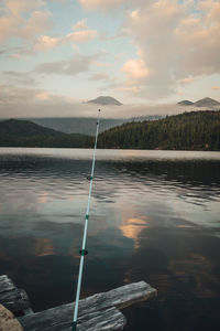 Fishing rod by lake against sky during sunset