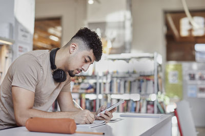 Male student taking notes in library