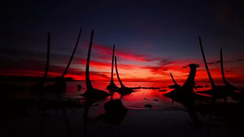 Silhouette sailboats moored in sea against orange sky