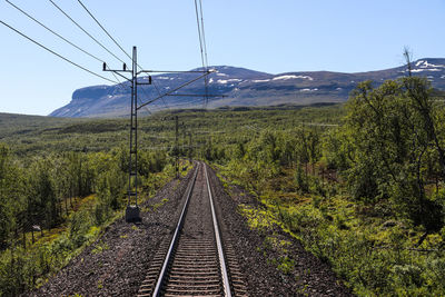 Railroad tracks by mountain against clear sky