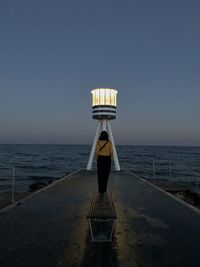 Woman walking against illuminated lighthouse at beach