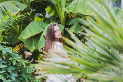 Portrait of young woman standing by banana leaf outdoors