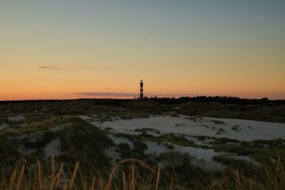 Silhouette lighthouse by sea against sky during sunset