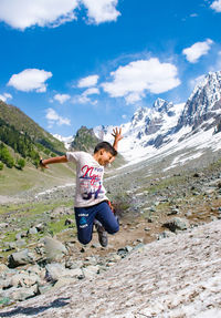 Rear view of boy jumping on mountain against sky