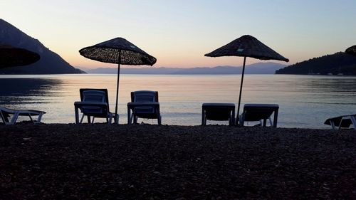 Chairs and tables on beach against sky during sunset