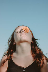 Low angle view of woman with flower on one eye against clear sky