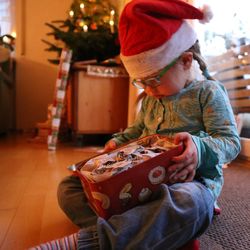 Cute girl wearing santa hat holding container while sitting at home