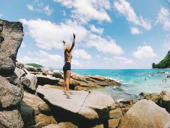 Man standing on rock by sea against sky