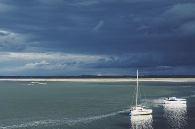 Boats sailing in river against cloudy sky